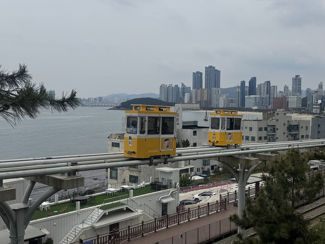 釜山海云台 Blue Line Park 高架轨道上的黄色天空胶囊车厢,背后是大海与城市