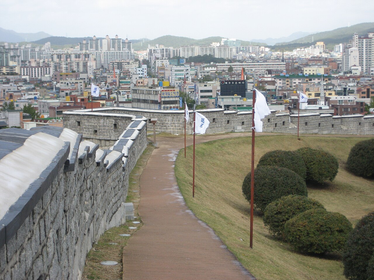 水原华城的石砌城墙步道与垛口,背后是现代城市